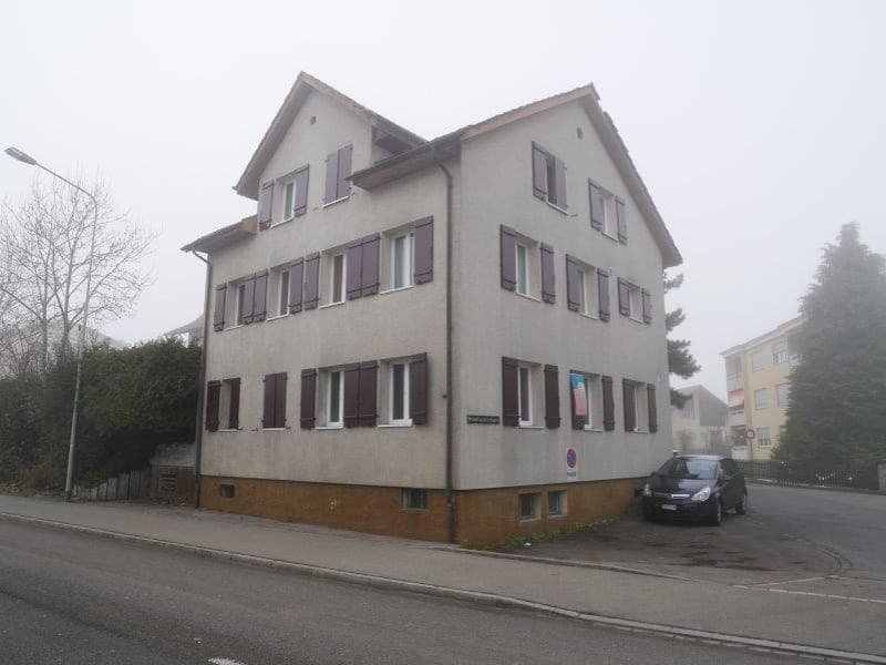 Gray apartment building with multiple windows, brown base, streetlight and parking in front
