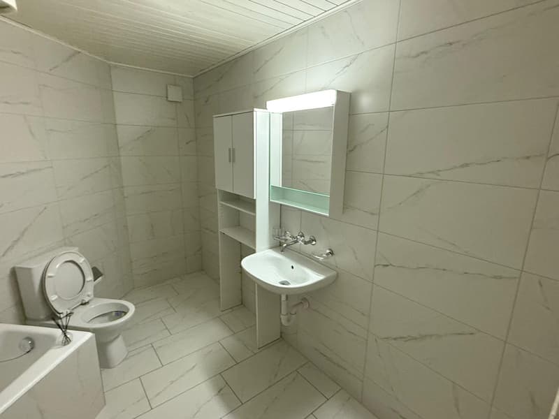A bathroom with white tiled walls, a toilet, a sink, a bathtub, a cabinet, and a mirror.
