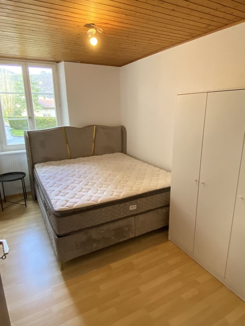 bedroom with bed, nightstand, wardrobe, wooden floor, white walls, window