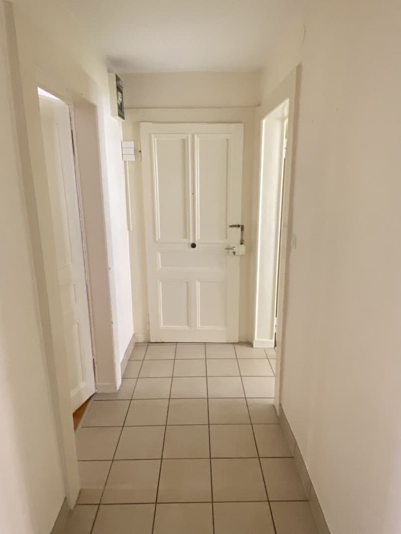 Empty hallway with tiled floor, white walls, and three doors