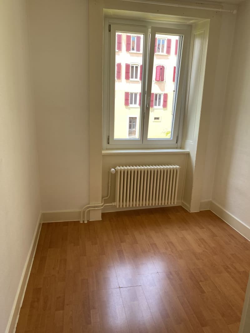 Room with wooden floor, empty, view of another building, radiator, window
