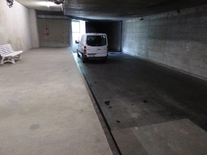Concrete garage interior with a white van parked inside. The garage has a concrete floor and walls.