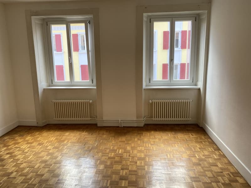 Empty room with hardwood flooring, two windows, and radiators along the walls