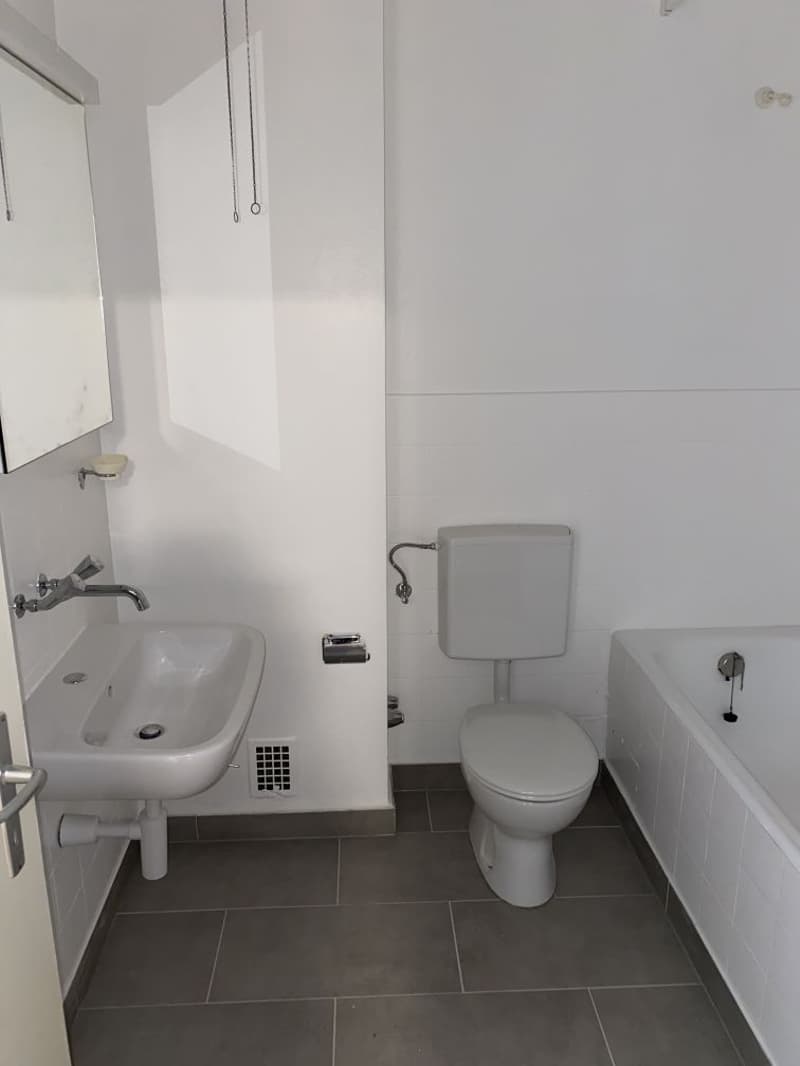 White bathroom with sink, toilet, and bathtub. Tile flooring and walls. Washing machine visible.
