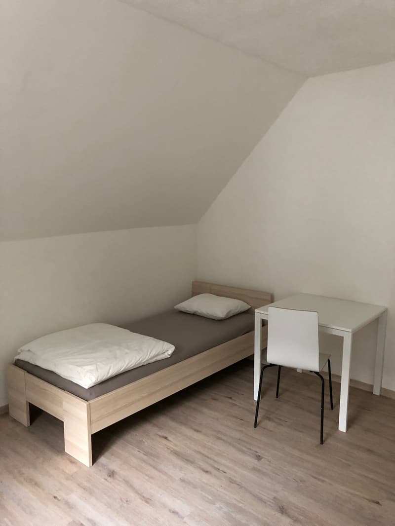 small room, bed with pillows, desk, white chair