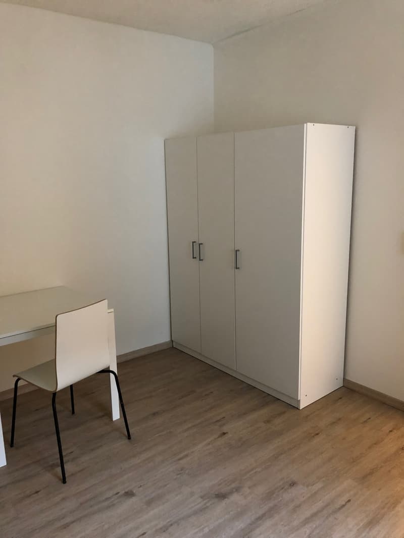 Empty room with a desk, chair, and a closet. Wooden floor and white walls.