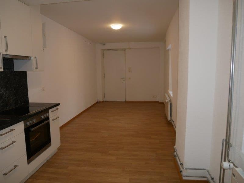 Open-plan studio apartment with hardwood flooring, white walls, kitchen with dishwasher, and a front door visible.