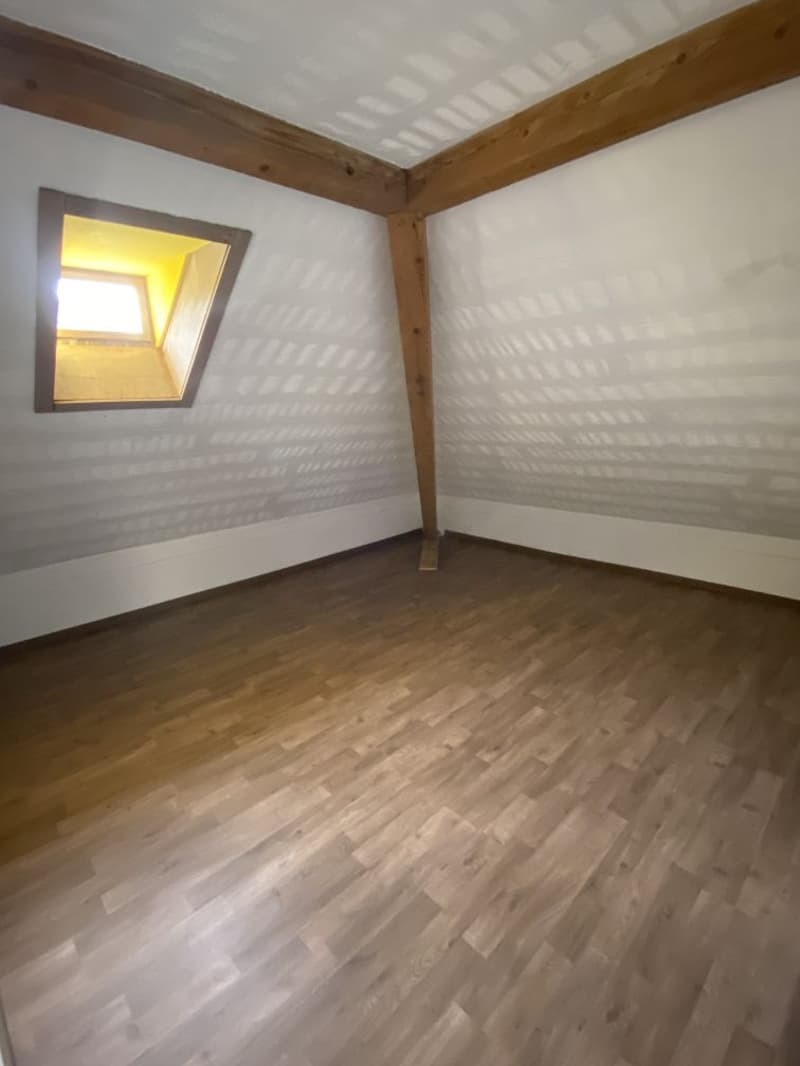 empty attic room with wooden beams, wooden floor, small window, slanted ceiling