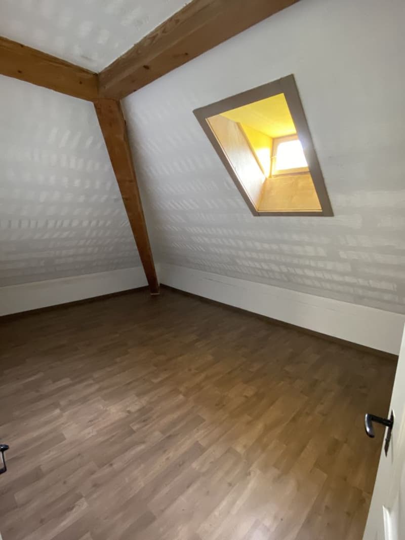 Empty attic room with wooden flooring and wooden beams, window at the ceiling