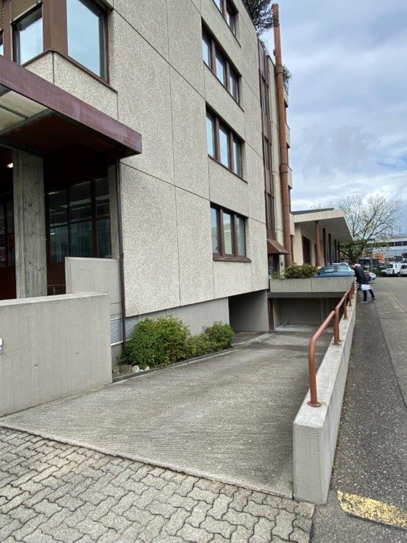 A multi-story building with a concrete entrance, garage, and paved access road.