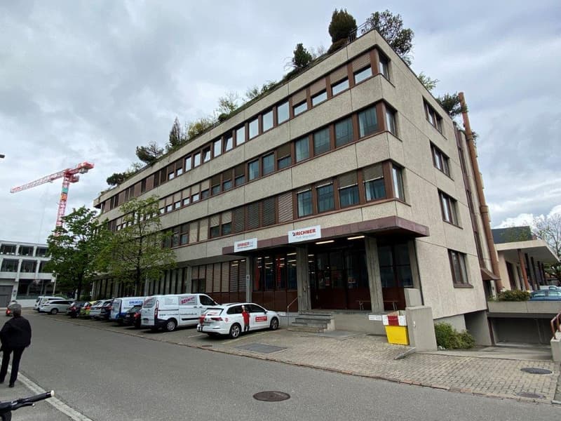 5 story building, many windows, multiple cars parked, signboard on front