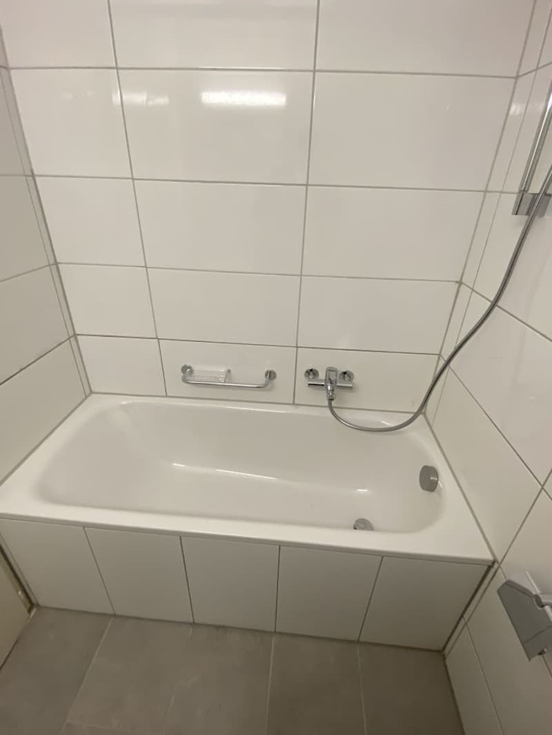 White tiled bathroom with a bathtub, shower curtain, and wall-mounted faucet