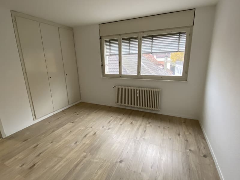 empty room, wooden floors, white walls, large window with blinds, built-in radiator