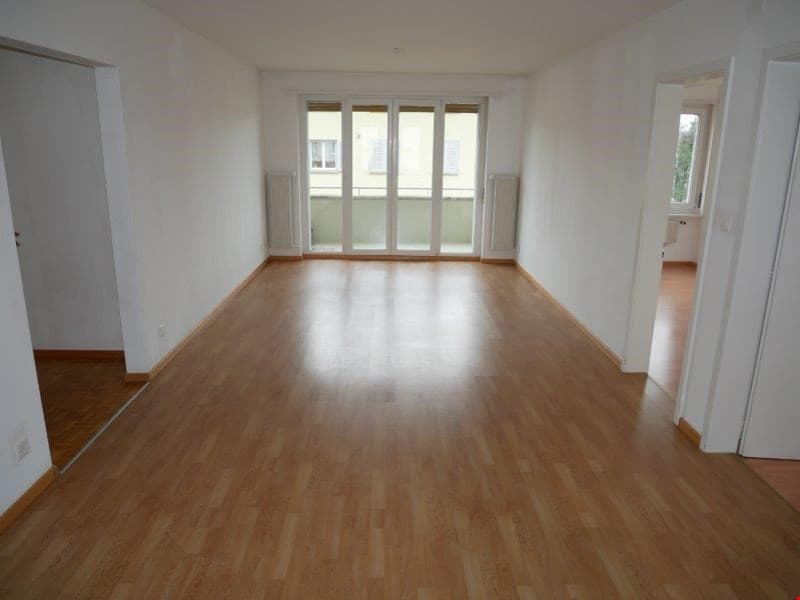 Empty room, wooden floor, sliding glass doors leading to balcony, white walls and ceiling