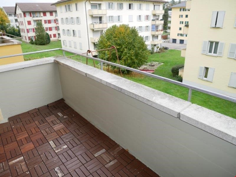 wooden deck, metal railing, grassy lawn, buildings in background