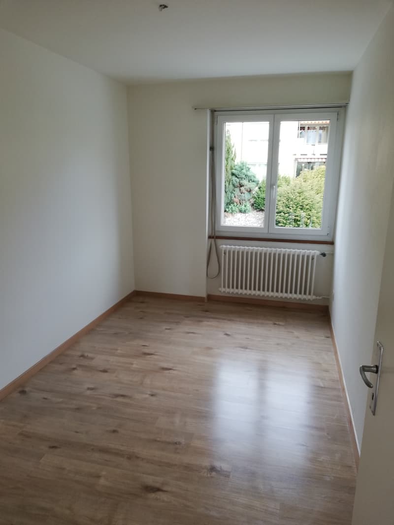 empty room with white walls, wooden floor, white radiator, window overlooking trees