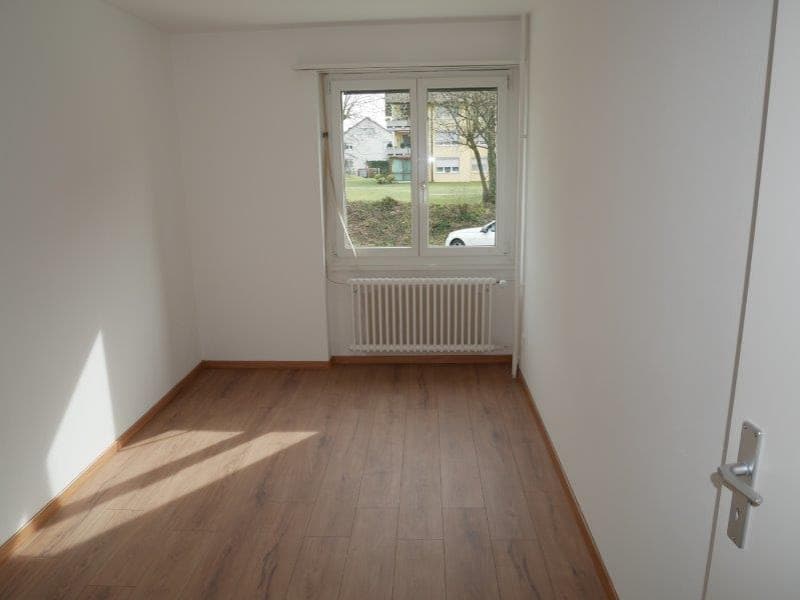 Spacious bedroom with hardwood flooring, large window providing natural light, and a radiator for heating.