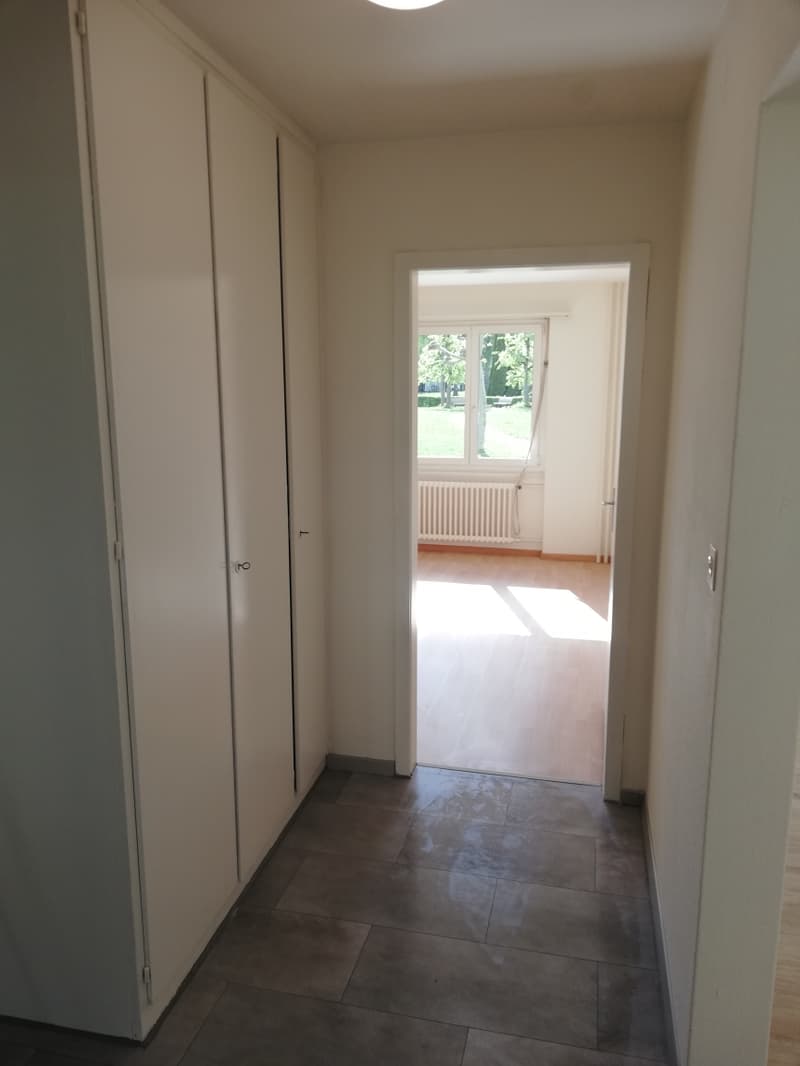Empty hallway with double doors, tiled floor, white walls, sunlight from the window, and a radiator