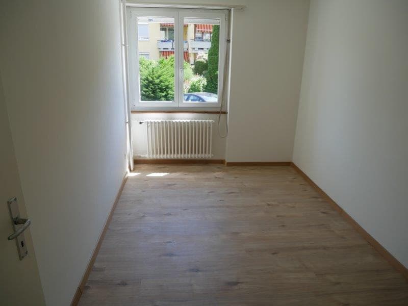 empty room, wooden floor, white walls, radiator, window with outside view, door on the left