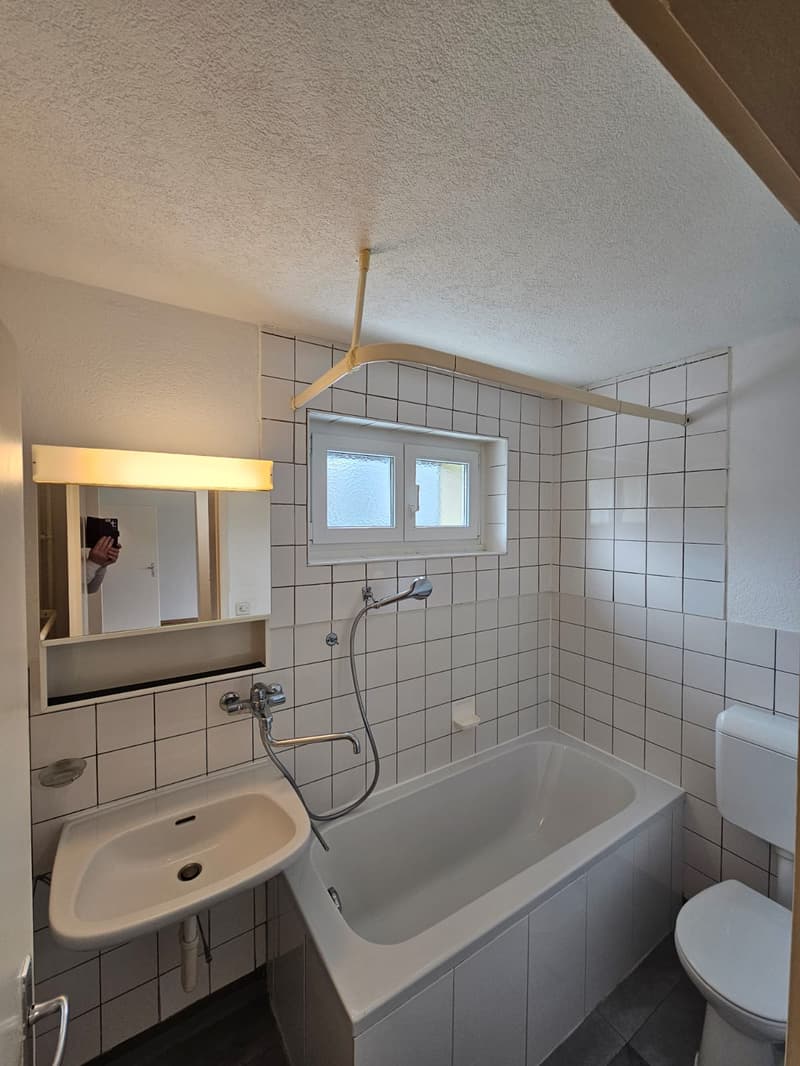 modern bathroom with white tiles, bathtub, sink, toilet, mirror with lighting, small window