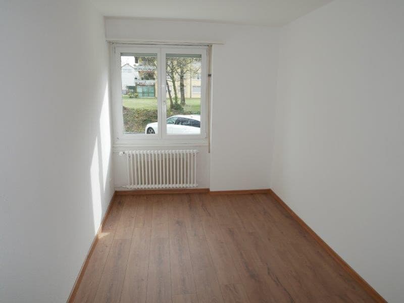 Spacious bedroom with large window, white walls, and hardwood flooring