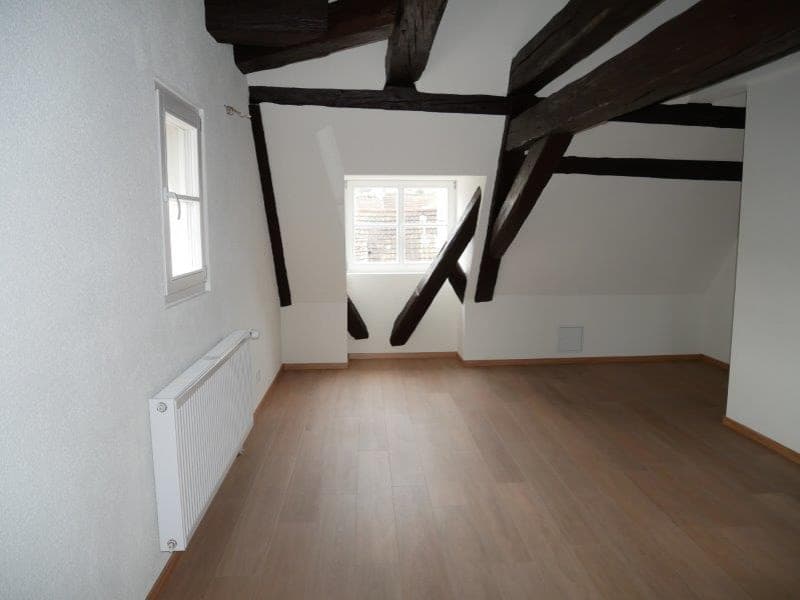 empty room with wooden floor, wooden beams, and white walls; two windows and a white radiator