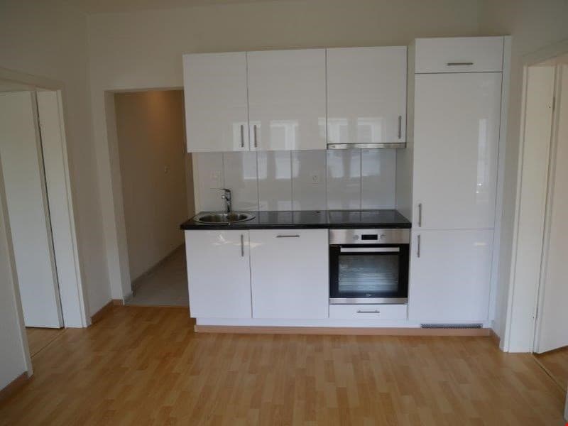 white cupboards, wooden floor, stainless steel oven, sink with faucet, black countertop