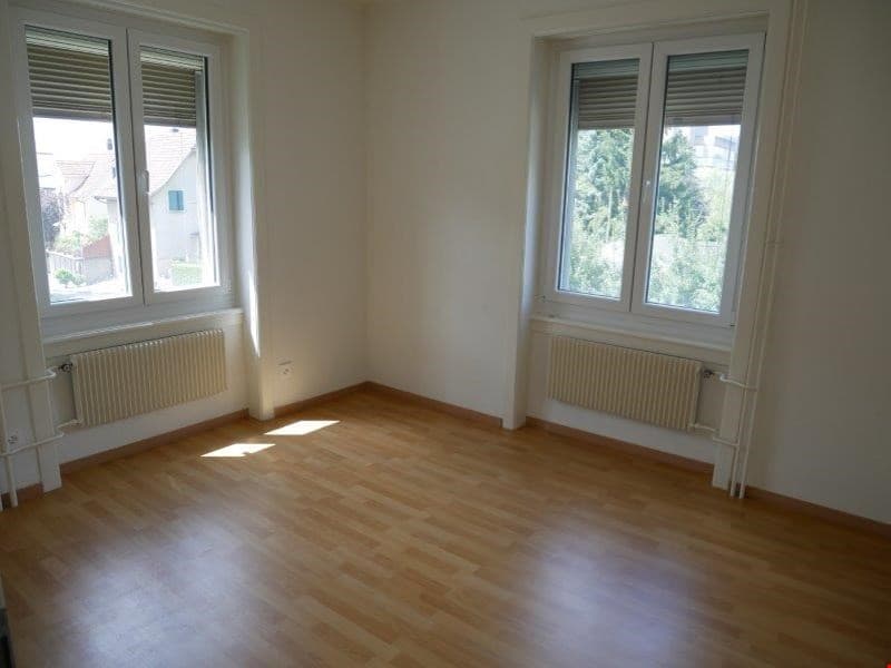 Empty room with hardwood floors, white walls, large windows, built-in white radiators