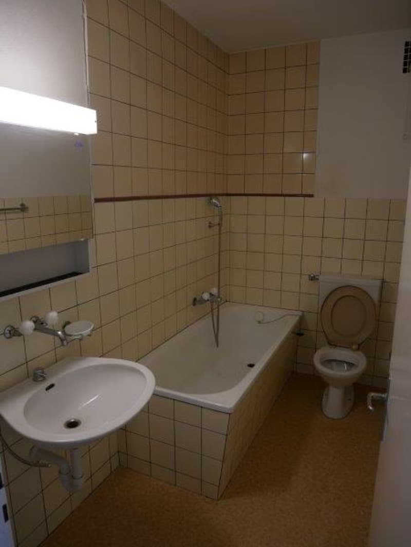 Tiled walls, tiled floor, bathtub, toilet, sink, and overhead lighting.