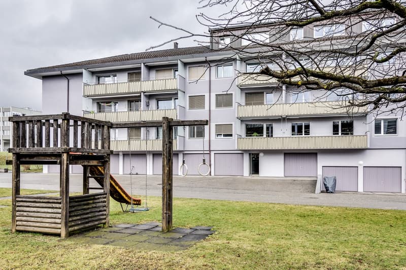 Multi-story apartment building, balconies, windows, slide, swings, garage doors, playground, tree