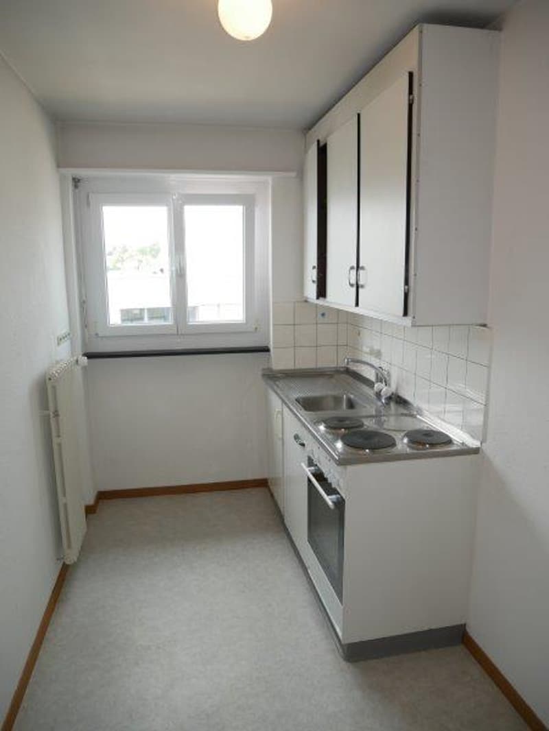 Empty kitchen with sink, stove, and window.