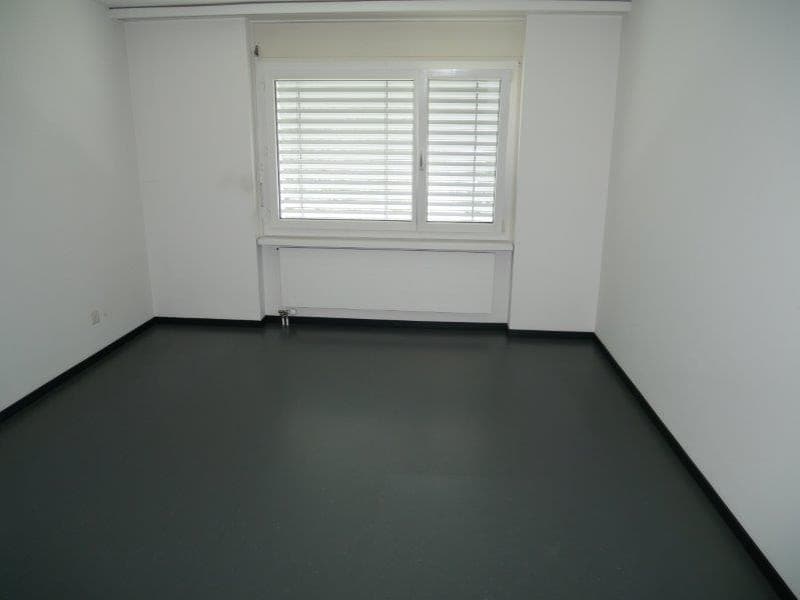 An empty room with white walls, a white radiator, a large window, and gray flooring
