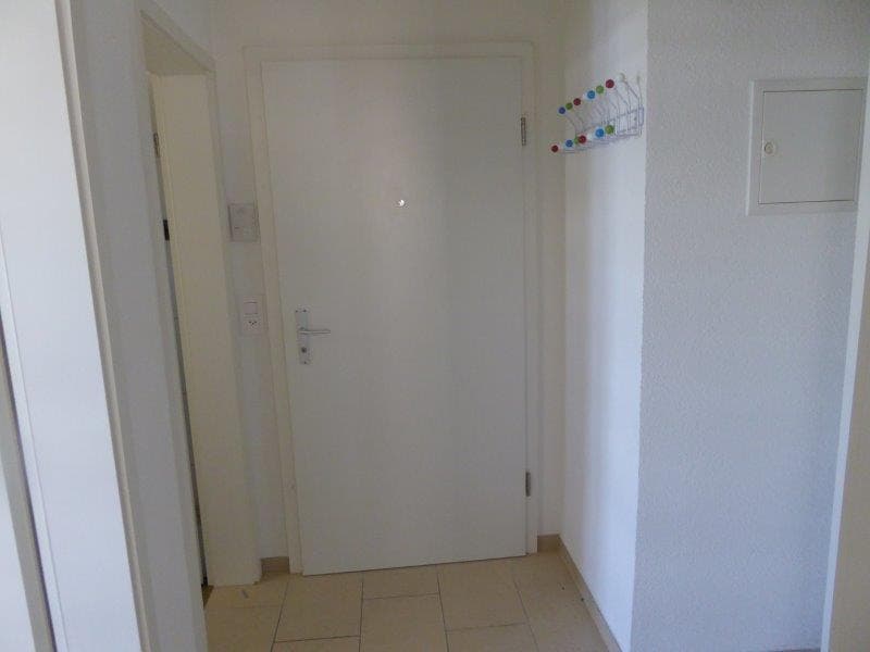 Corridor with white walls, white tile flooring, white door, power outlet, coat rack on the wall