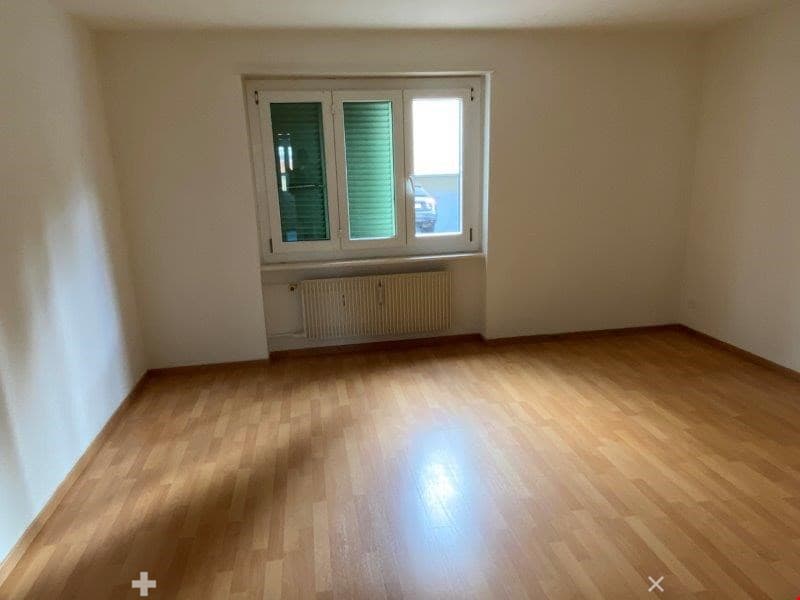 Empty room, white walls, wooden floor, large window with white frame and green shutters, white radiator