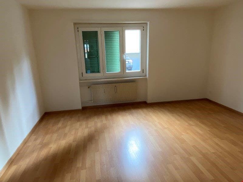 Empty room, white walls, wooden floor, large window with white frame and green shutters, white radiator