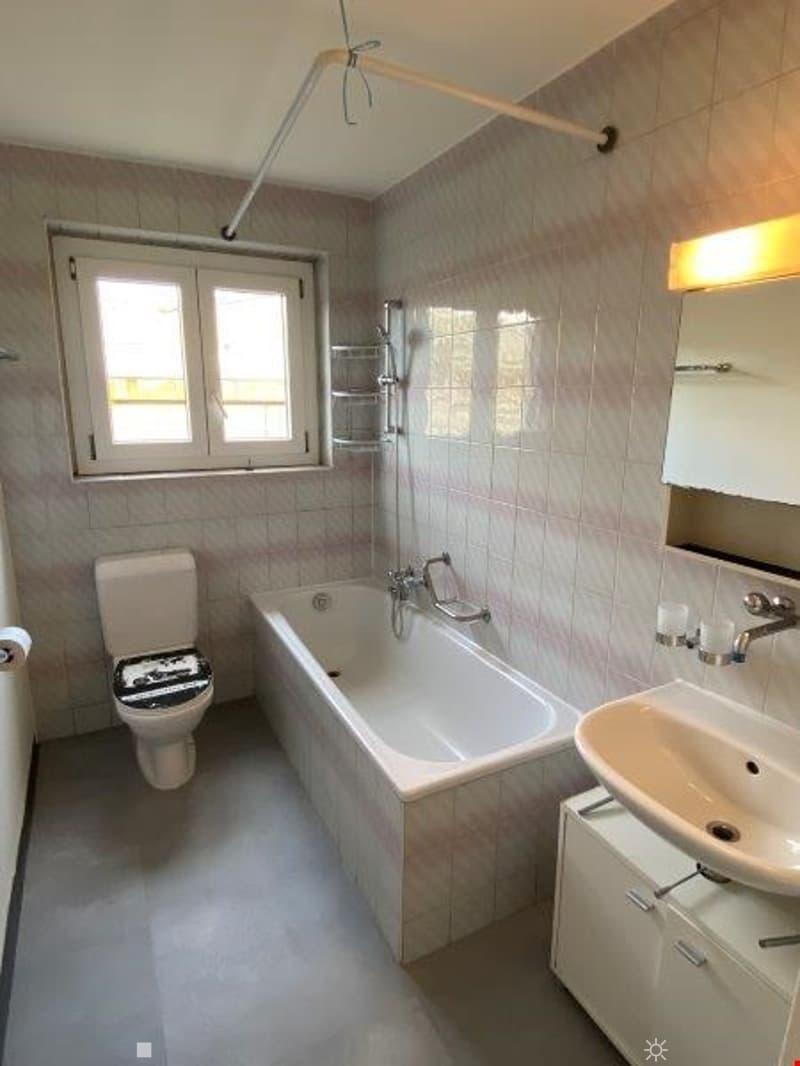 a bathroom with a white bathtub, white toilet, white sink, and a mirror with a light