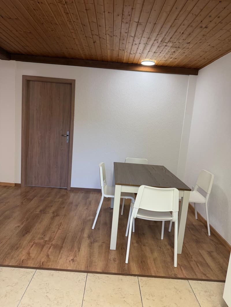 small room with wooden floors, white walls, wooden ceiling, table with 4 chairs, white table, wooden door
