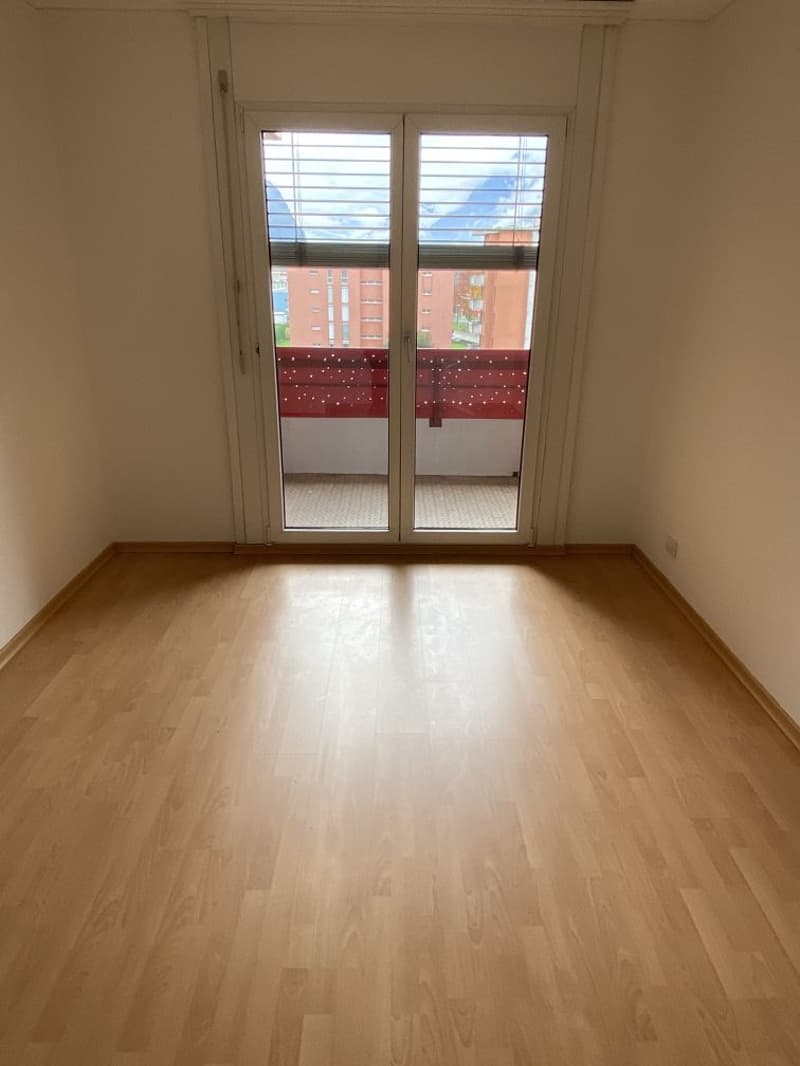 wooden floor, empty room, double sliding glass doors leading to balcony, red railing on balcony