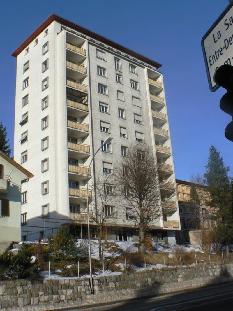 apartment building with 4 floors, multiple balconies, street lamp, snowy hill, stone wall