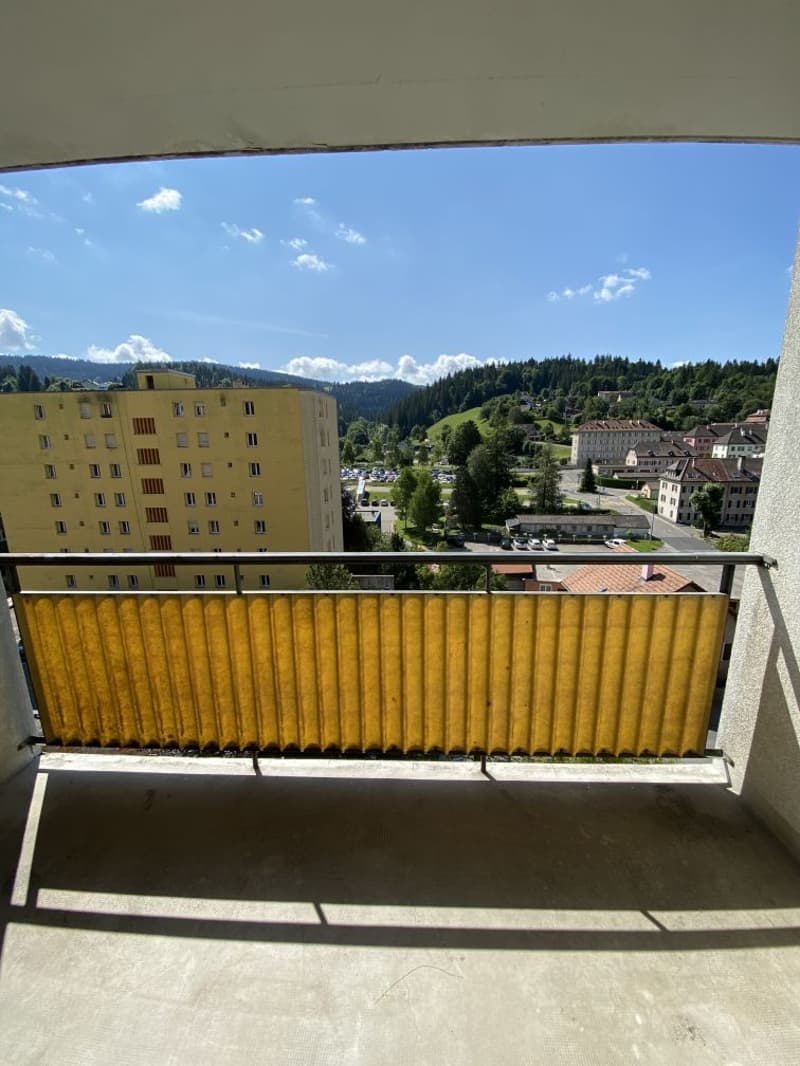 Balcony with metal railing, yellow shade, concrete floor, view of the city and mountains