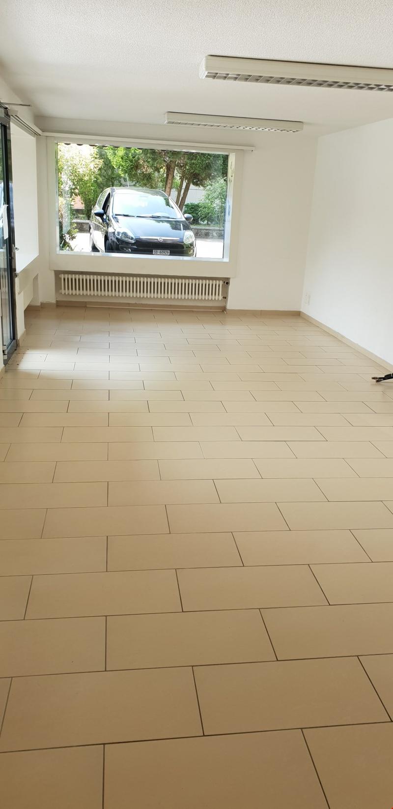 Empty room with white walls, beige tiles, large window, car visible outside