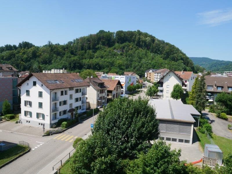Aerial view of a residential area with several buildings, a parking lot, and a mountain in the background.