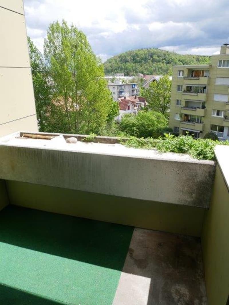Balcony with green carpet, concrete railing, view of trees and buildings