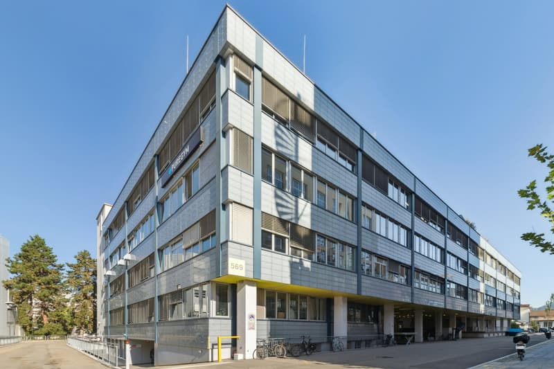 modern office building, multiple windows, gray exterior, yellow accents, multiple bicycles parked, street in front