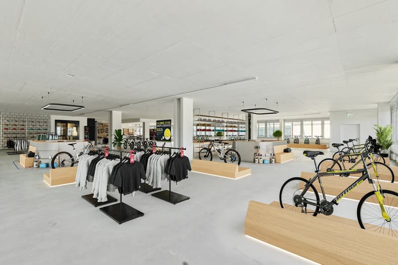 An indoor area with bicycles on display, clothes on racks, benches, plants, and a counter.