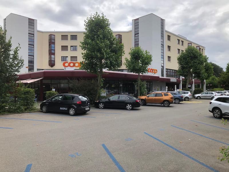 Multi-story commercial building with a Coop supermarket on the ground floor, surrounded by a parking lot with several cars parked