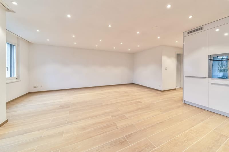 Empty kitchen with modern design, wooden flooring, built-in cabinets, a single built-in oven, and a large window.