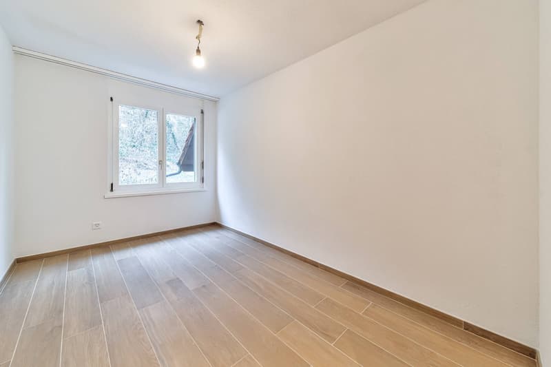 empty room with wooden floor, white walls, one window with an outside view