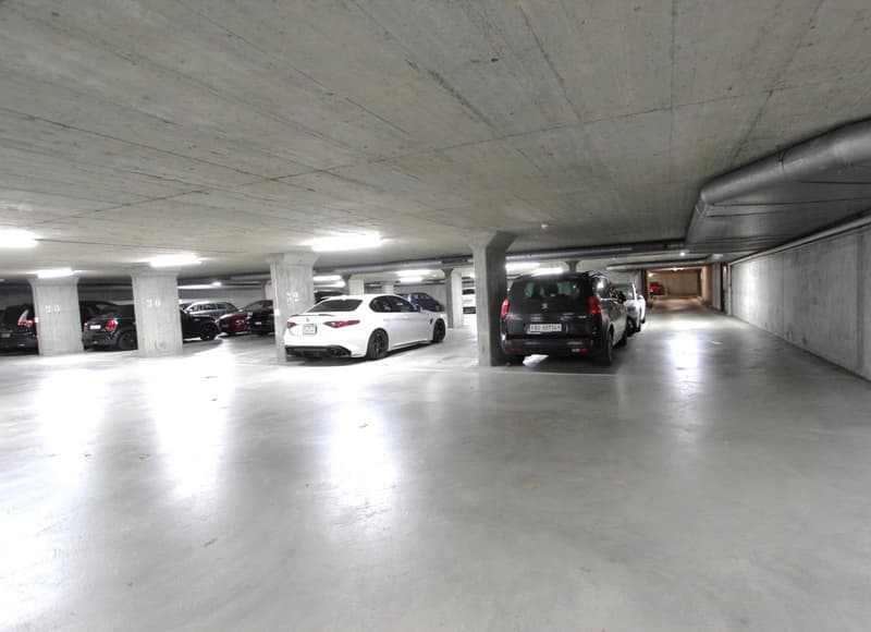 underground parking lot with concrete walls and columns, fluorescent lighting, multiple vehicles parked