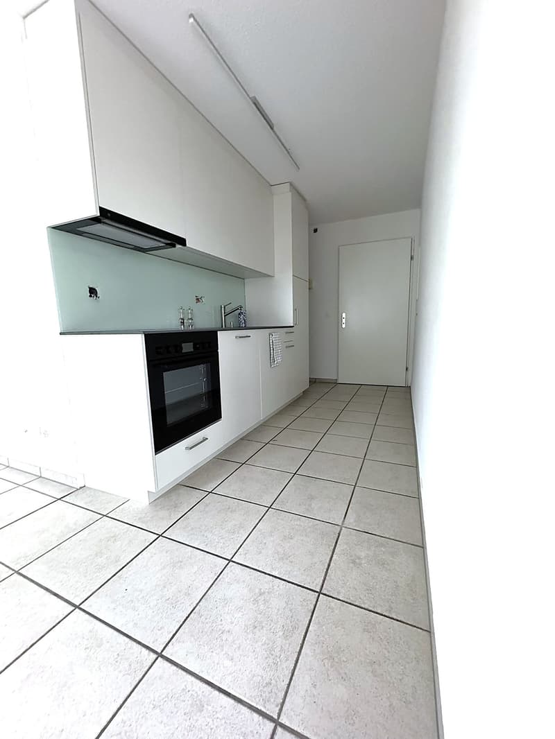 modern kitchen with white tiles, black oven, glass splashback, white cabinetry, sink with faucet, glass and metal decorative items, door at end